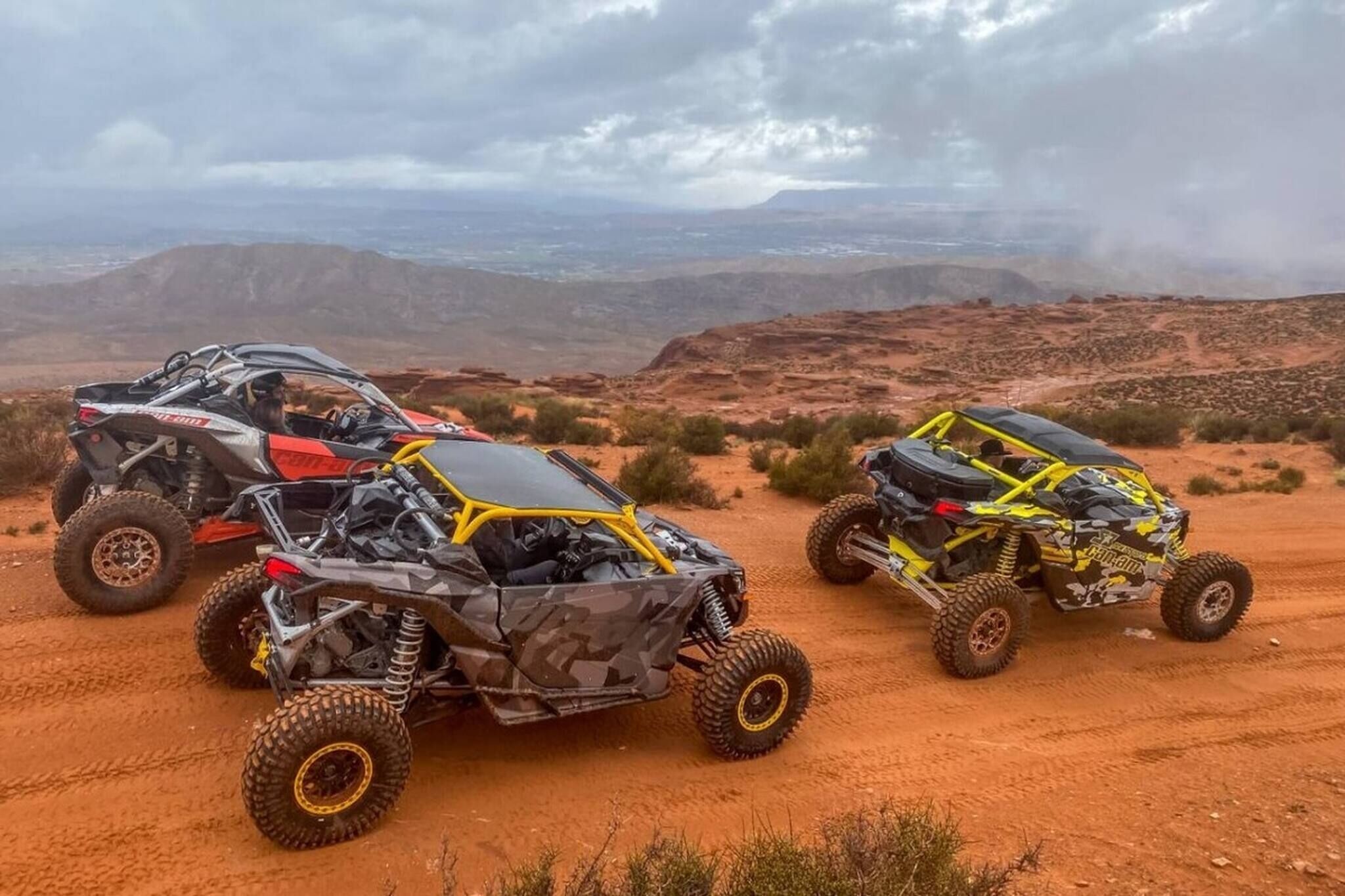 Three off-road vehicles parked on a dirt road with a mountainous landscape in the background.