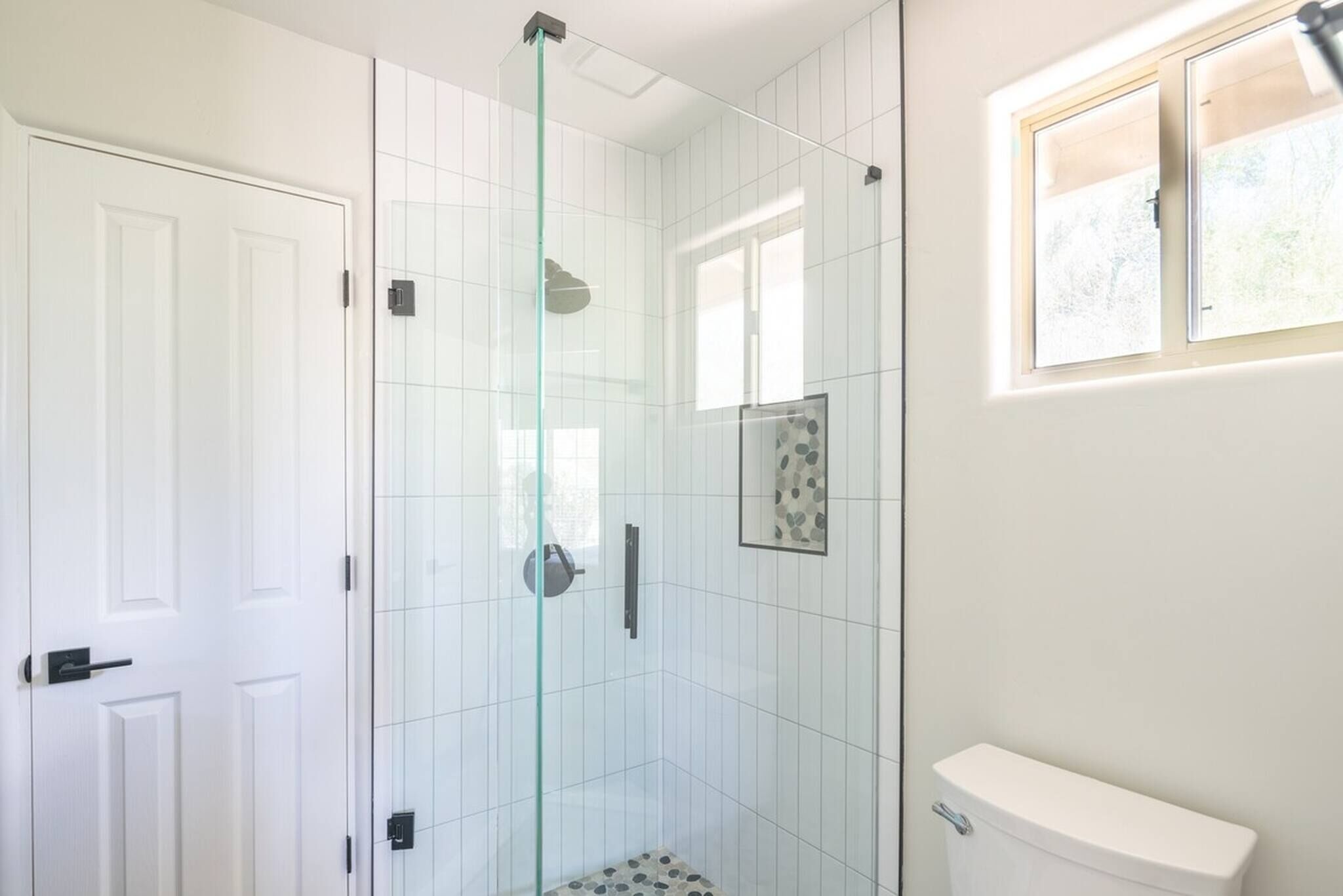 A bathroom with a glass shower enclosure, a toilet, and a window.