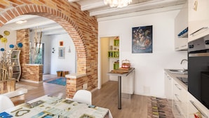 Una cocina moderna con un arco de ladrillo, una zona de comedor con una mesa cubierta con un mantel estampado, y un cuadro en la pared.