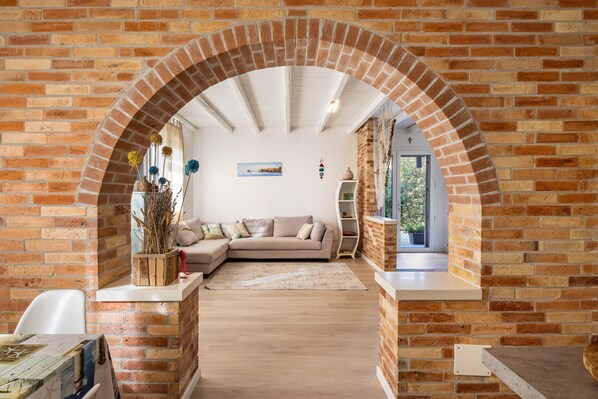 A living room with a brick archway, a beige sofa, a wooden coffee table, and a white chair.
