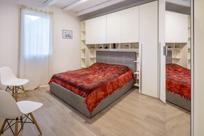 Een slaapkamer met een bed, een bureau, twee stoelen, een kledingkast en een spiegel.