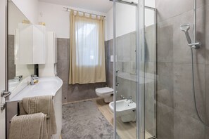 Een moderne badkamer met een douchecabine van glas, een witte wastafel en een toilet.