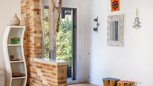 Una habitación con pared de ladrillo, estante blanco curvo, puerta corredera de vidrio, un espejo y dos taburetes de madera.