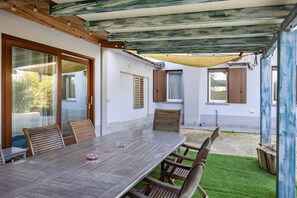 An outdoor dining area with a table and chairs, a wooden ceiling, and a grassy lawn.