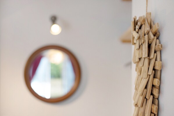 A round mirror on a wall, a wooden wall hanging, and a ceiling light fixture.
