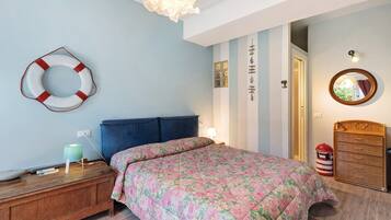 A bedroom with a bed, bedside table, lamp, dresser, and a wall-mounted mirror.