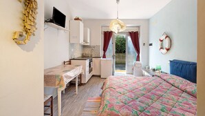 Ein kompakter Raum mit Bett, Schreibtisch, Küchenzeile und Zugang zu einem Außenbereich.