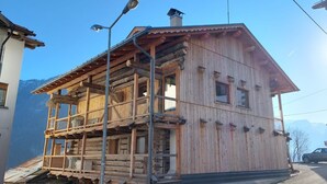 A wooden chalet with a balcony, a chimney, and a mountain backdrop.