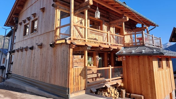 A wooden chalet with a balcony, a small porch, and a chimney.