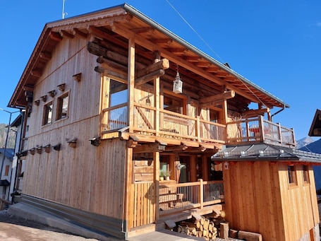 A wooden chalet with a balcony, a small porch, and a chimney.