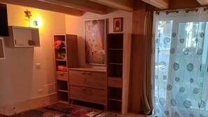 A room with a wooden floor, a red sofa, a patterned rug, a wooden cabinet, and a painting on the wall.