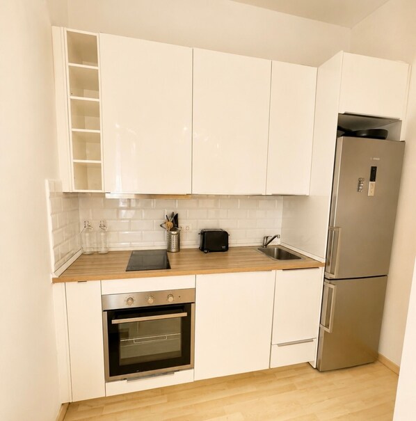 Una cocina con armarios blancos, un refrigerador de acero inoxidable, horno empotrado y encimera de madera.