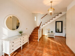 Ein Flur mit Treppe, einem runden Spiegel, einer weißen Konsole und einem kleinen Tisch mit Lampe.