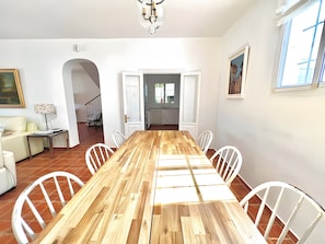 A dining area with a wooden table, white chairs, a sofa, and a staircase leading to another room.