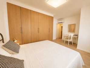 Ein Schlafzimmer mit einem großen Bett, einem Holzschrank, einem Schreibtisch, einem Stuhl und einer Klimaanlage.