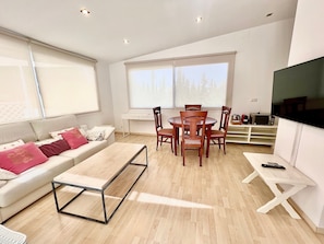 A modern living room with a sofa, dining table, chairs, a TV, and a coffee table.