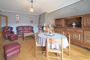 Une pièce avec une table ronde, des chaises en bois, un canapé en cuir rouge, une cheminée et un buffet en bois.