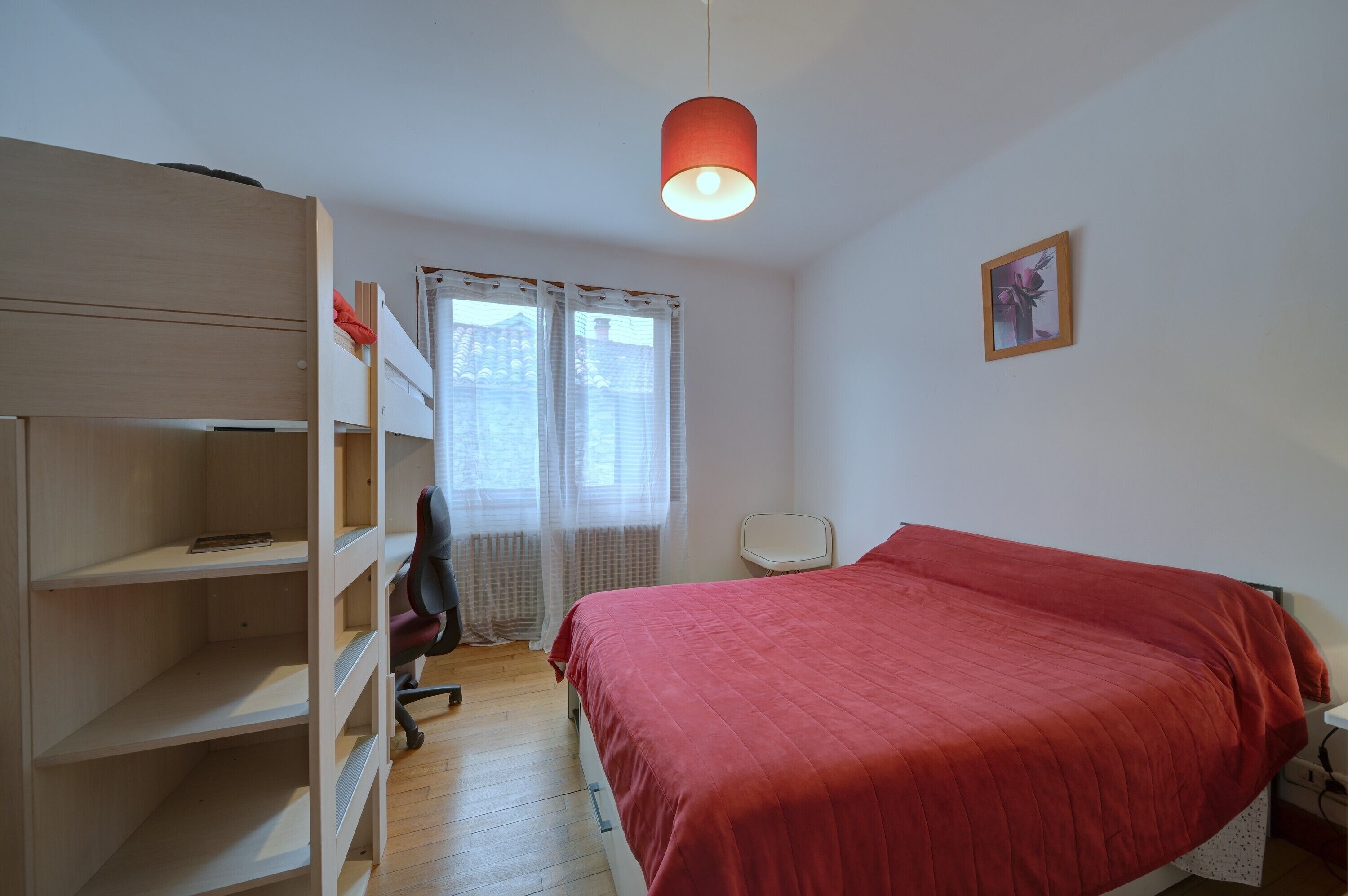 A bedroom with a bed, a desk, a chair, a wardrobe, and a window with curtains.
