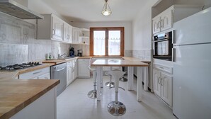 A modern kitchen with white cabinetry, a wooden countertop, and a central island with bar stools.