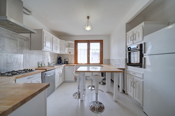 Une cuisine moderne avec des meubles blancs, un plan de travail en bois et un îlot central doté de tabourets de bar.