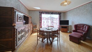 A dining area with a round table and chairs, a red leather armchair, a television, and a radiator.
