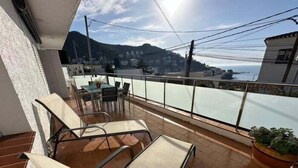 A balcony with a table and chairs, a potted plant, and a view of a town and mountains. - Lovely flat near the beach, terrace AV-04 (Roses)