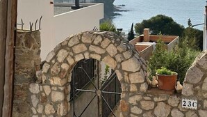 A stone archway with a metal gate, a potted plant, and a house number '23C'. - Lovely flat near the beach, terrace AV-04 (Roses)
