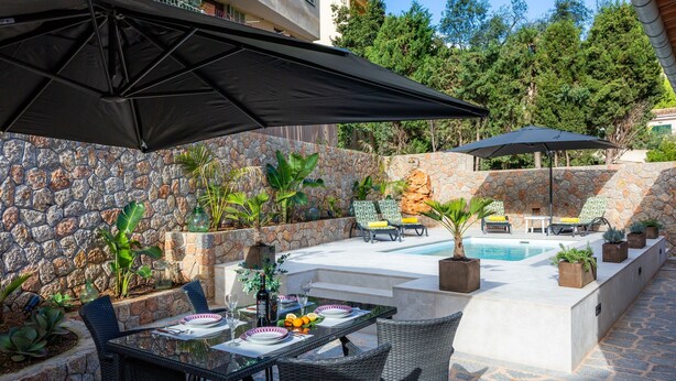 An outdoor patio with a stone wall, a pool, and a table set for dining. - Villa Puerto Apartment with Mountain Views, Pool, and Wi-Fi (Sóller)