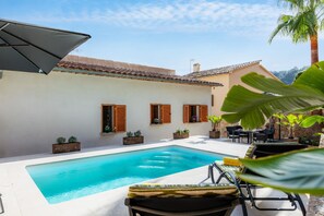Piscina com espreguiçadeiras, mesa e plantas em vasos.