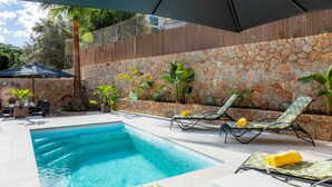 A swimming pool with lounge chairs and umbrellas, surrounded by a stone wall and plants. - Villa Puerto Apartment with Mountain Views, Pool, and Wi-Fi (Sóller)