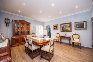 Uma área de refeições com mesa e cadeiras de madeira, um armário com portas de vidro e obras de arte emolduradas nas paredes.