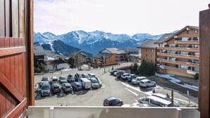 A view from a window overlooking a parking lot with cars and a building with a balcony. - Lovely vacation home Séjour grand ski (Huez)