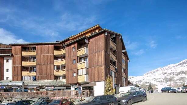 A multi-story hotel with balconies, a mountain backdrop, and a parking area. - Lovely vacation home Séjour grand ski (Huez)