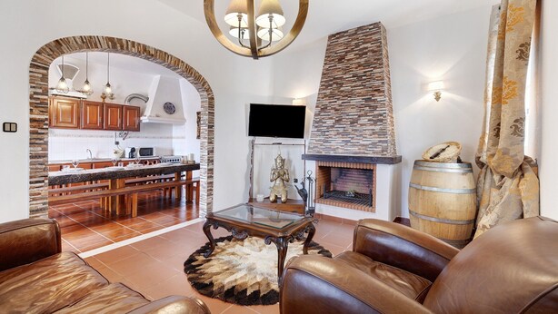 Un salon moderne avec des canapés en cuir, une table basse en verre, une cheminée et une cuisine dotée de meubles en bois et d’un mur d’accent en pierre.