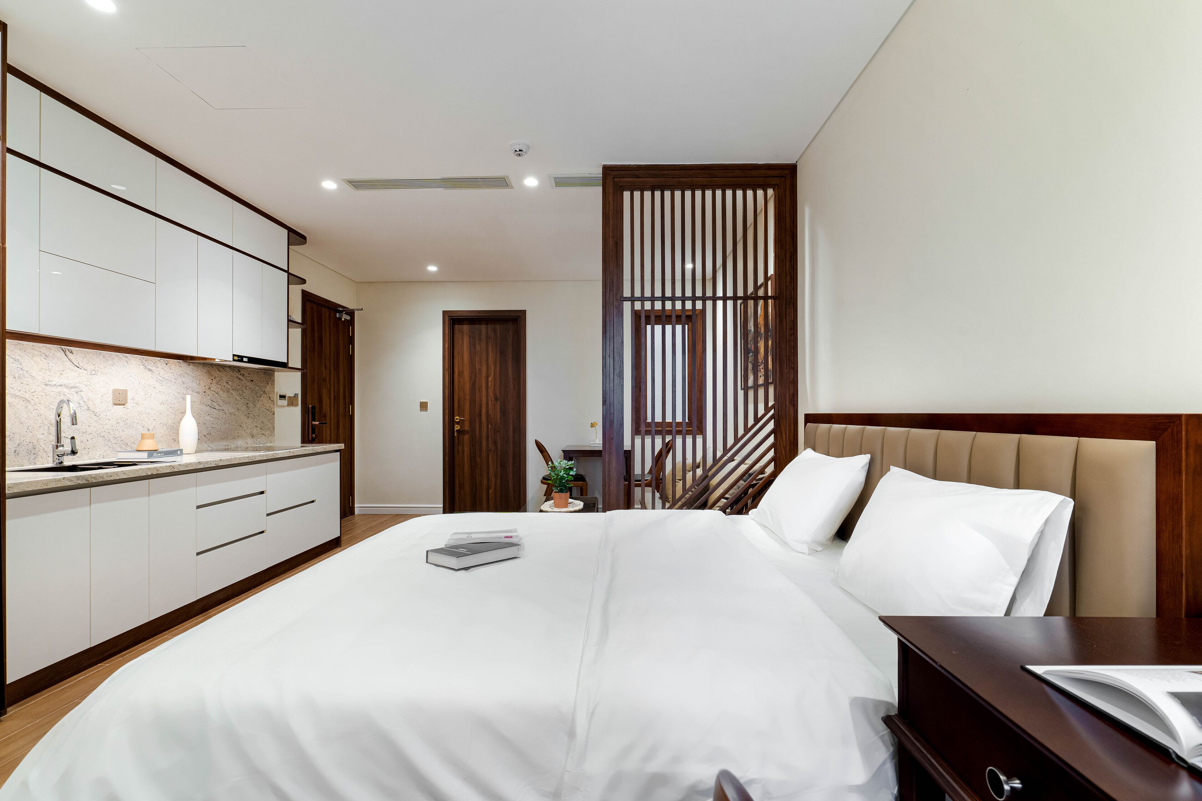 Moderni hotellihuone, jossa on suuri sänky, puinen pääty, yöpöytä ja sisäänrakennettu vaatekaappi.