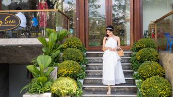 A woman in a white dress standing on stone steps with potted yellow flowers.