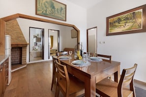 A dining area with a wooden table set for four, flanked by chairs, with a brick fireplace and a painting above. - Casa Verdelho – Retreat Among Vineyards with Lounge, Playground, and Shared Pool (Palmela)