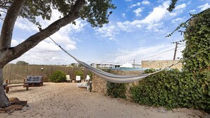 A hammock between trees, a stone wall, and a sandy area with lounge chairs. - Casa Verdelho – Retreat Among Vineyards with Lounge, Playground, and Shared Pool (Palmela)