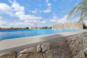 A swimming pool with a stone wall, a palm tree, and a building in the background. - Casa Verdelho – Retreat Among Vineyards with Lounge, Playground, and Shared Pool (Palmela)