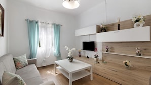 A modern living room with a sofa, a coffee table, a TV, and a wooden wall with shelves. - Casa Verdelho – Retreat Among Vineyards with Lounge, Playground, and Shared Pool (Palmela)