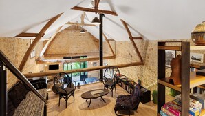 Um quarto estilo loft com vigas de madeira aparentes, uma mesa central, cadeiras e uma estante.