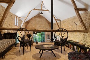 Una habitación rústica con vigas de madera a la vista, una mesa redonda, dos sillas, un sofá y una estantería llena de libros.