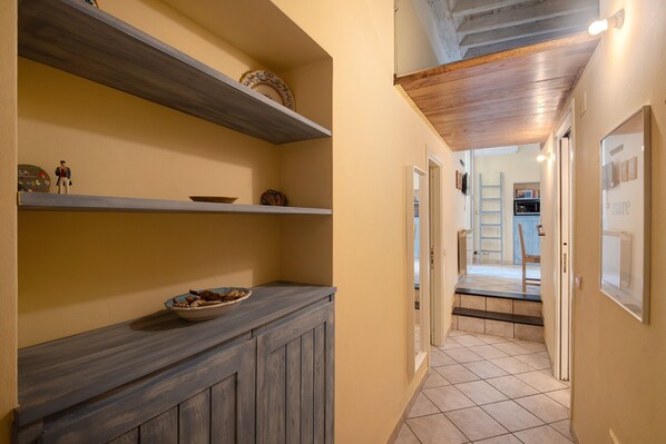 A hallway with wooden shelves, a bowl on a counter, and a view into another room.