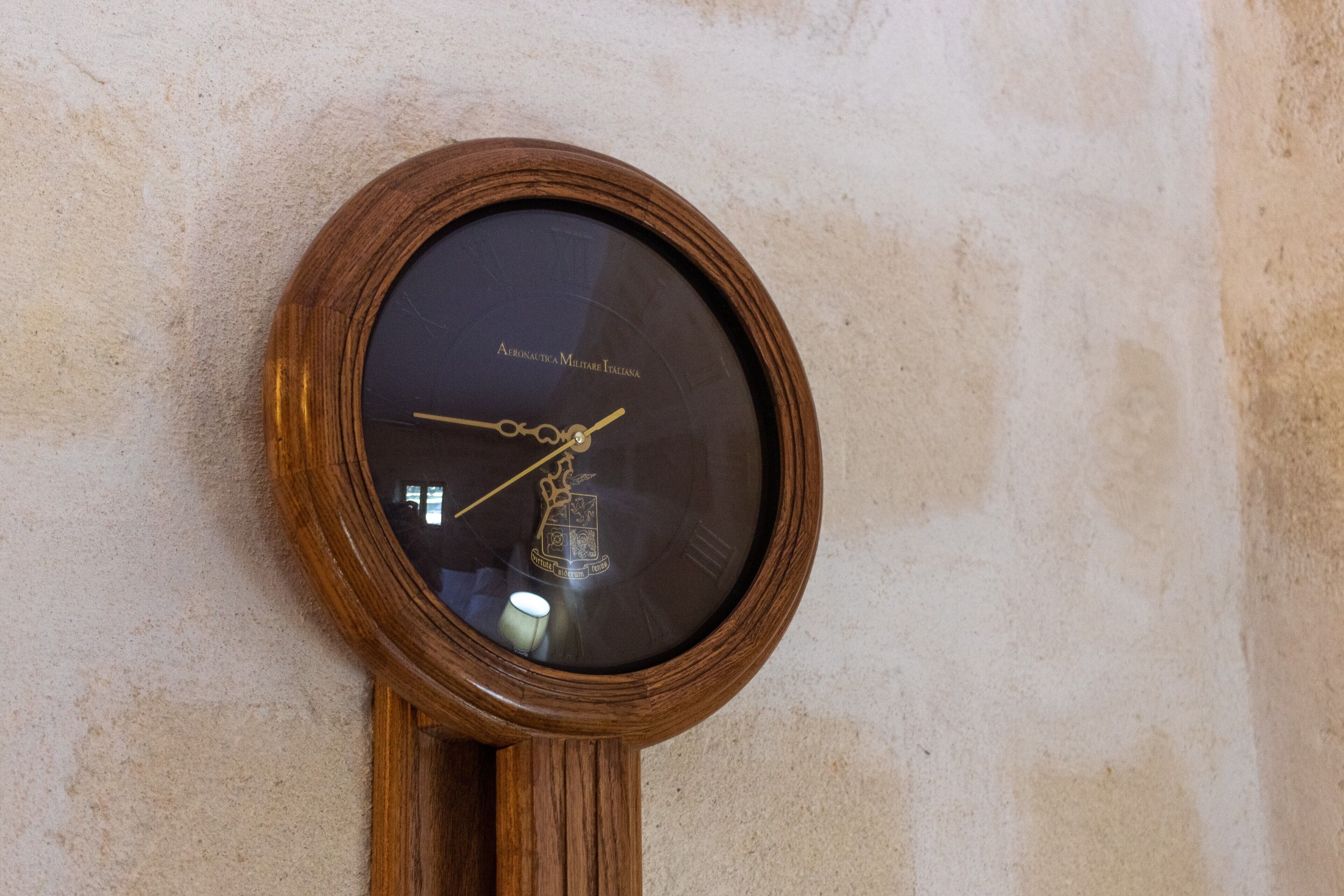 Eine an der Wand befestigte Uhr mit Holzrahmen und schwarzem Zifferblatt, mit römischen Ziffern und einem Pendel.