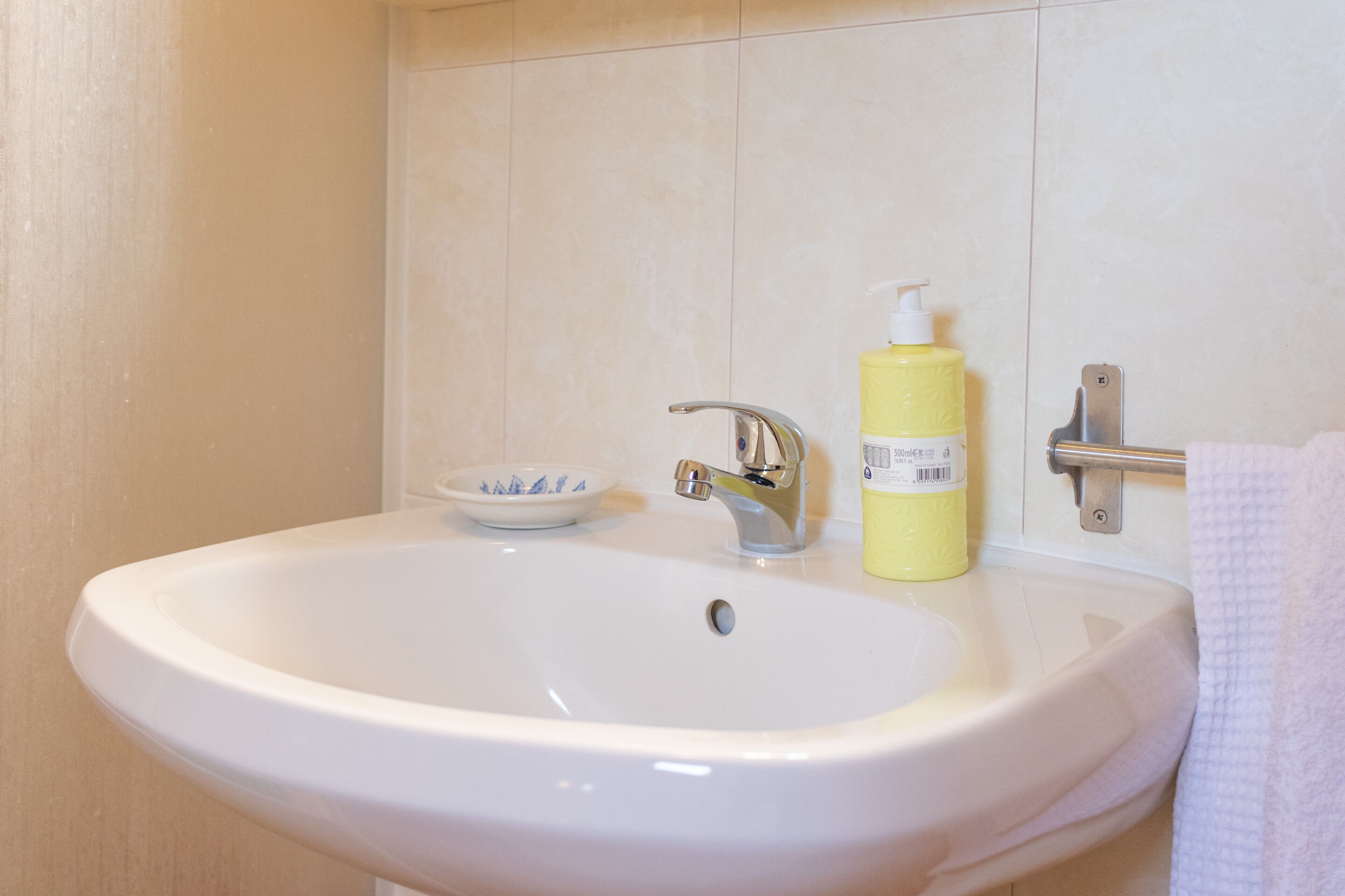 A bathroom with a white sink, a small bowl, and a yellow bottle of soap.