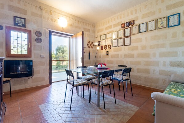 A dining area with a table and chairs, a television, and a sofa.