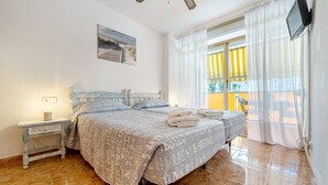 Camera da letto con un letto, comodino, lampada, ventilatore a soffitto, finestra con tende e TV a parete.