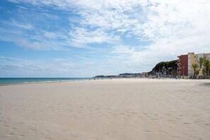 A beach with a clear sky, a sandy shore, and buildings in the background.