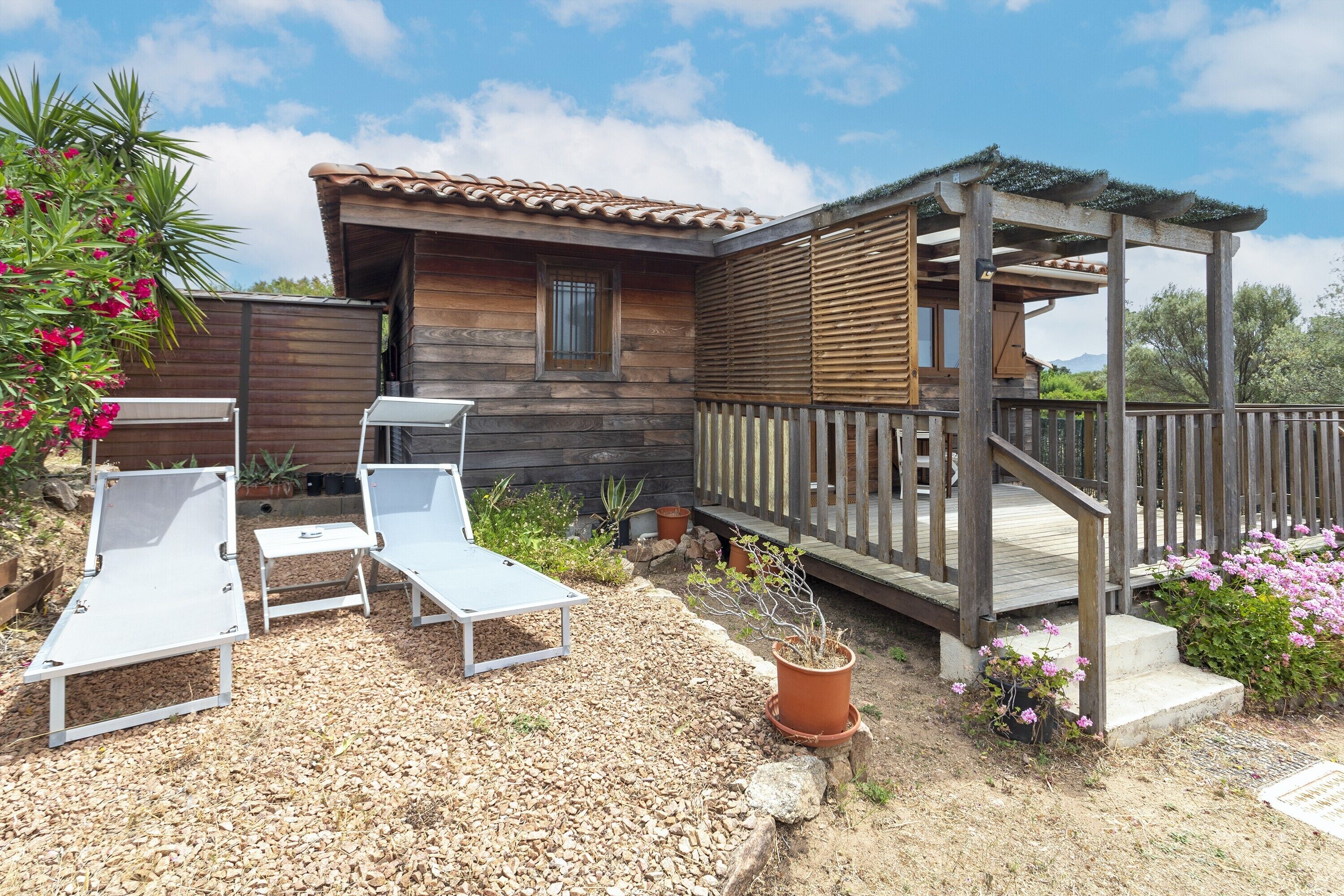 A wooden cabin with a patio area, including two lounge chairs and a small table.