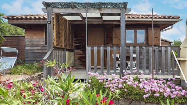 Une maison en bois avec un porche, une clôture en bois et un jardin où poussent des fleurs roses.